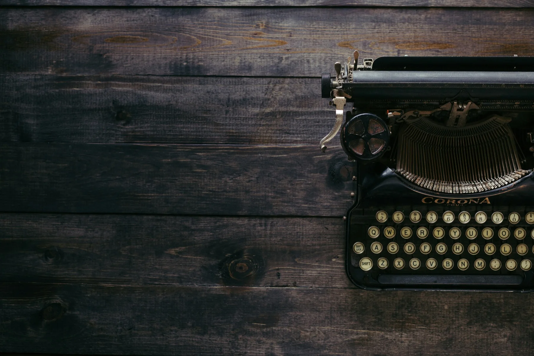 A black vintage typewriter on a dark wooden desk.